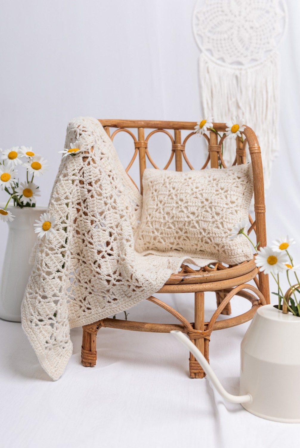 Dream Nest crochet baby blanket and matching lace pillow styled on a rattan chair with daisies