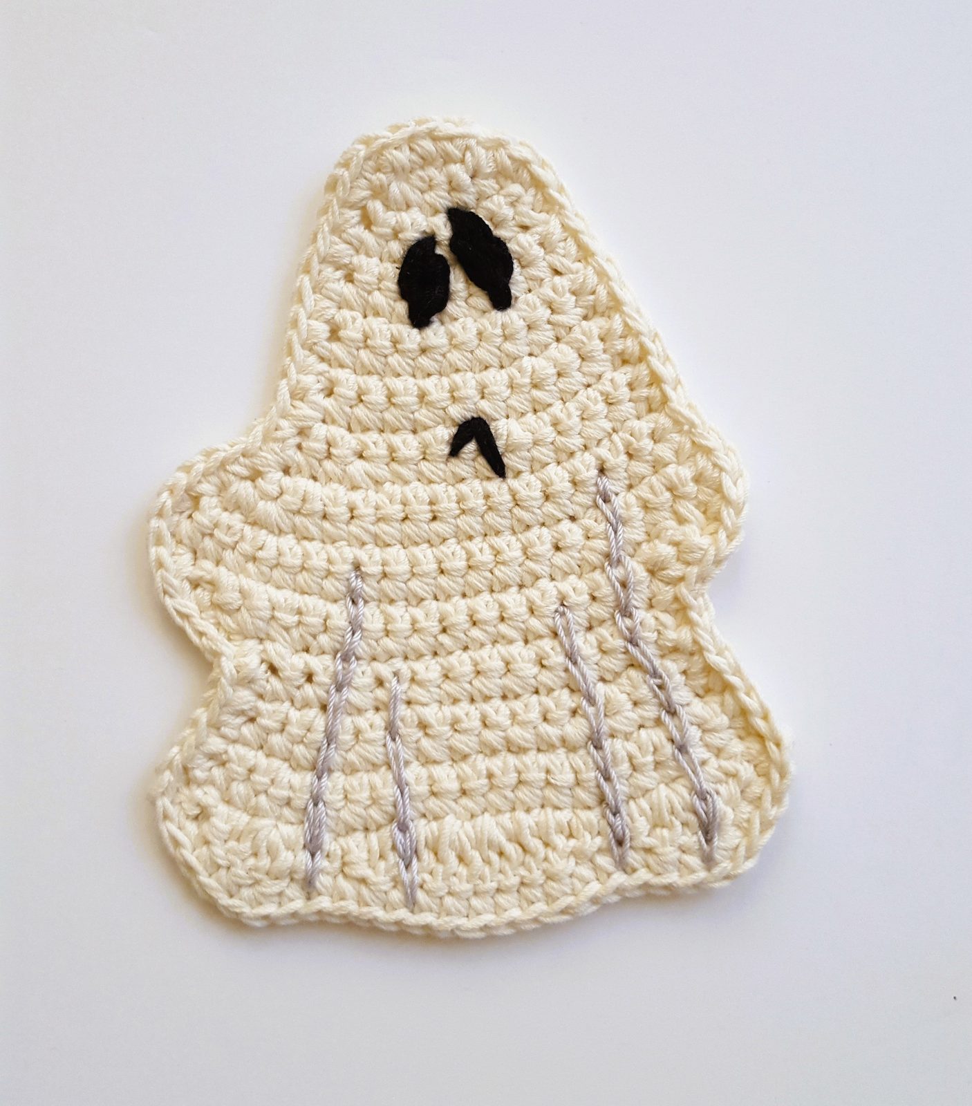 Cream crochet ghost coaster with an embroidered face, flat lay on a white background