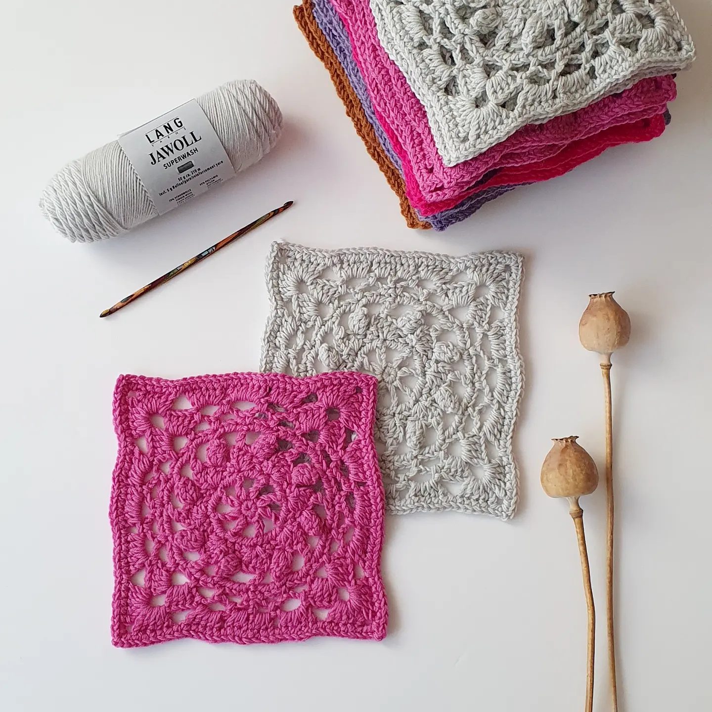 A ball of Lang Yarns Jawoll with a crochet hook, a stack of finished Holi squares, and two squares laid flat