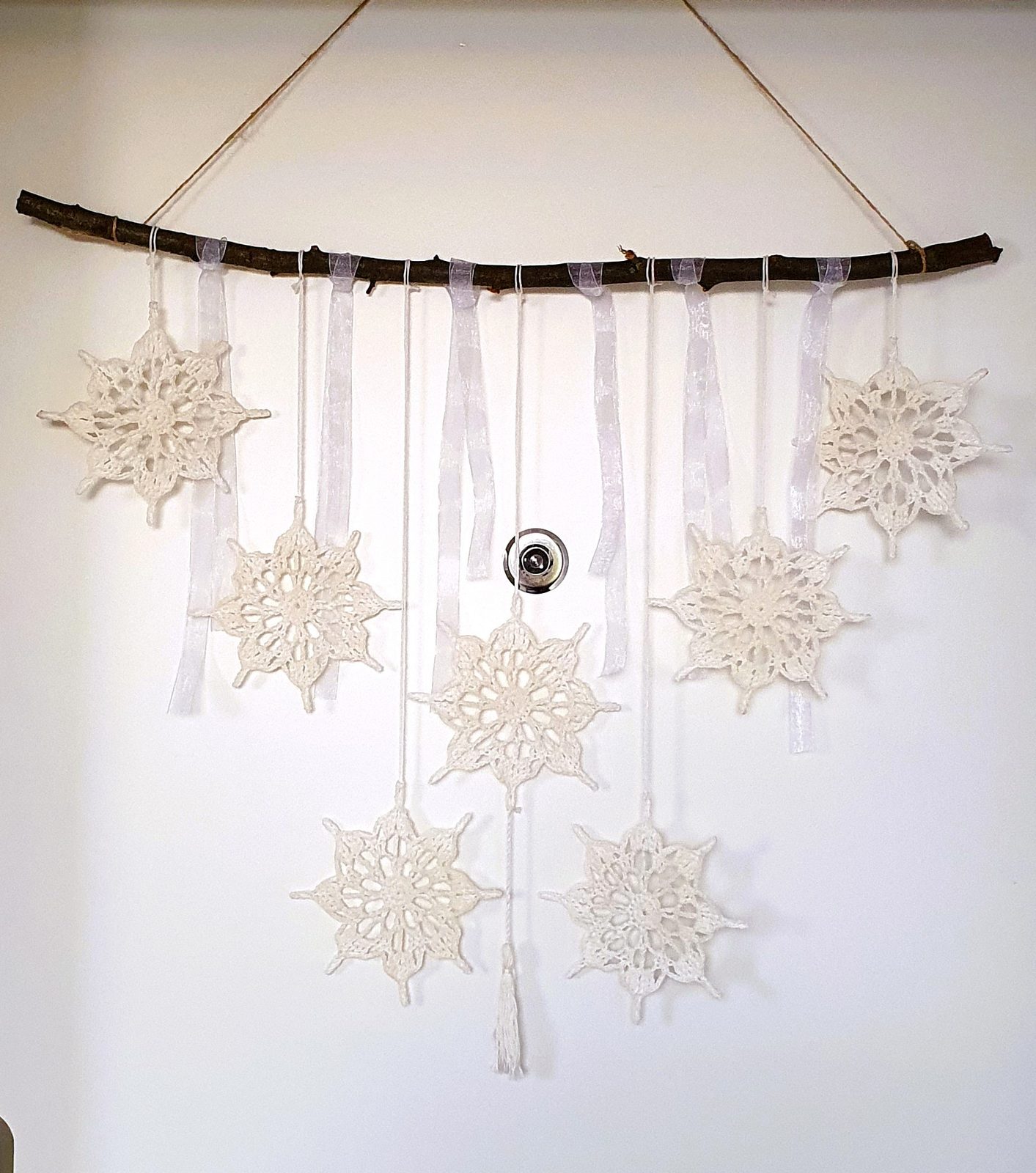 Seven cream lace crochet snowflakes hung on ribbons from a real branch, wall-mounted garland