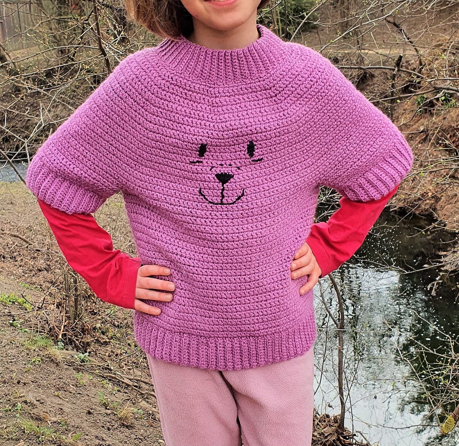 Teddy Bear Kids crochet sweater worn by a girl outdoors, front view showing the embroidered bear face